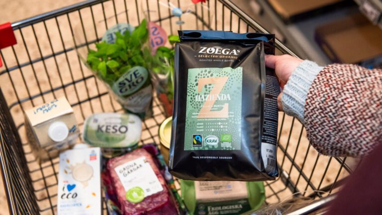En hand lägger när en påse med Zoegas KRAV-märkta kaffe i en kundvagn där det redan ligger en del varor.